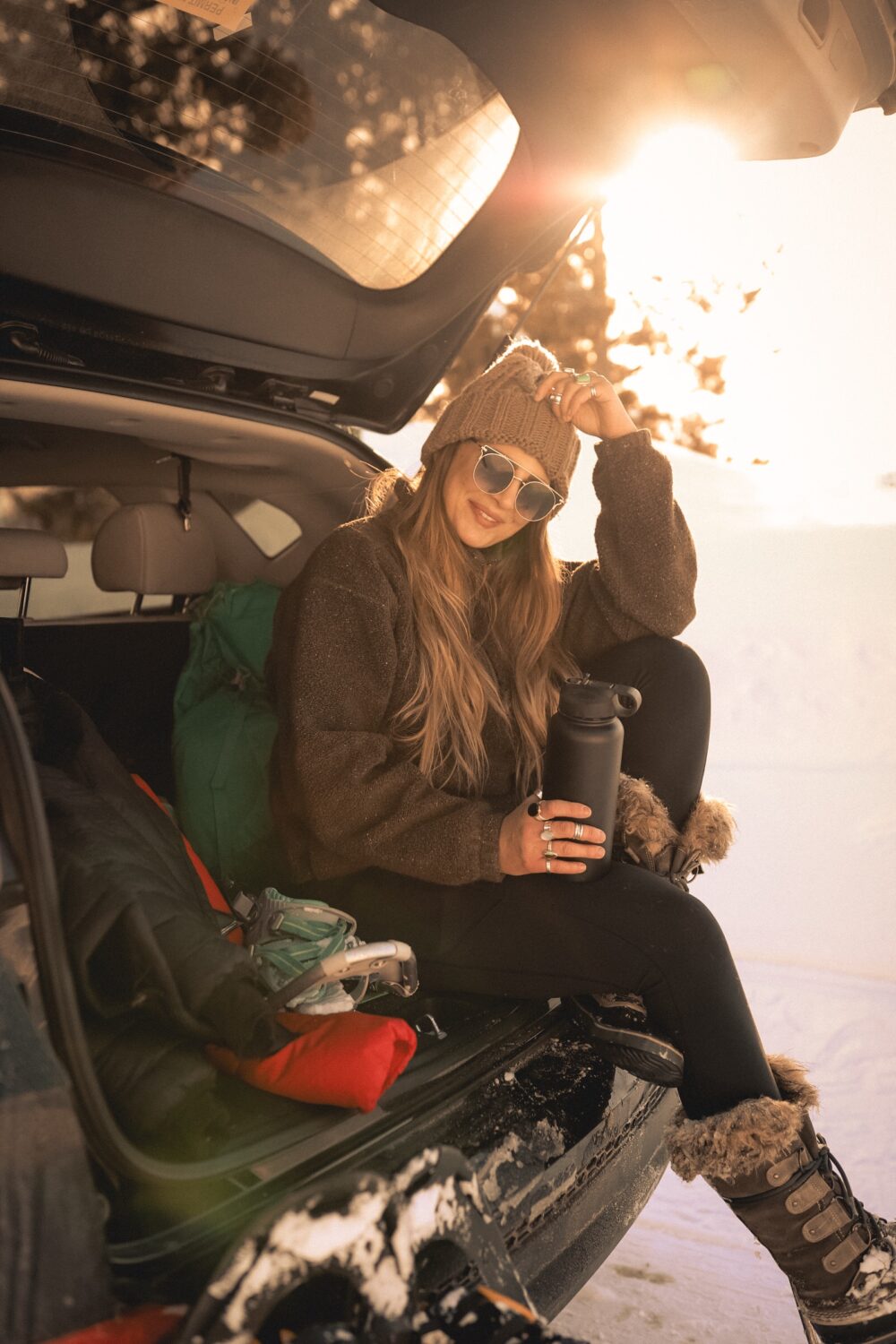 A woman in ski gear, sitting on the edge of her car.