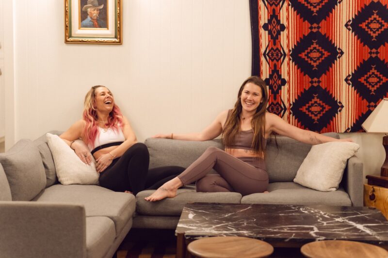 Two women laughing on the communal sofa in the Cache House lobby.