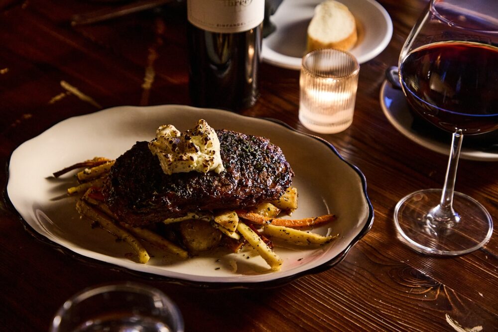 A steak with compound butter on top of roasted veggies.